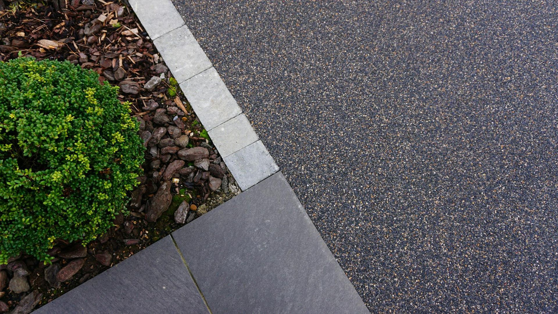 A close up of a concrete driveway with a bush in the background.