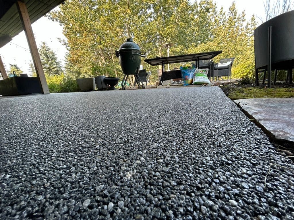A patio with a grill, table, and chairs on it.