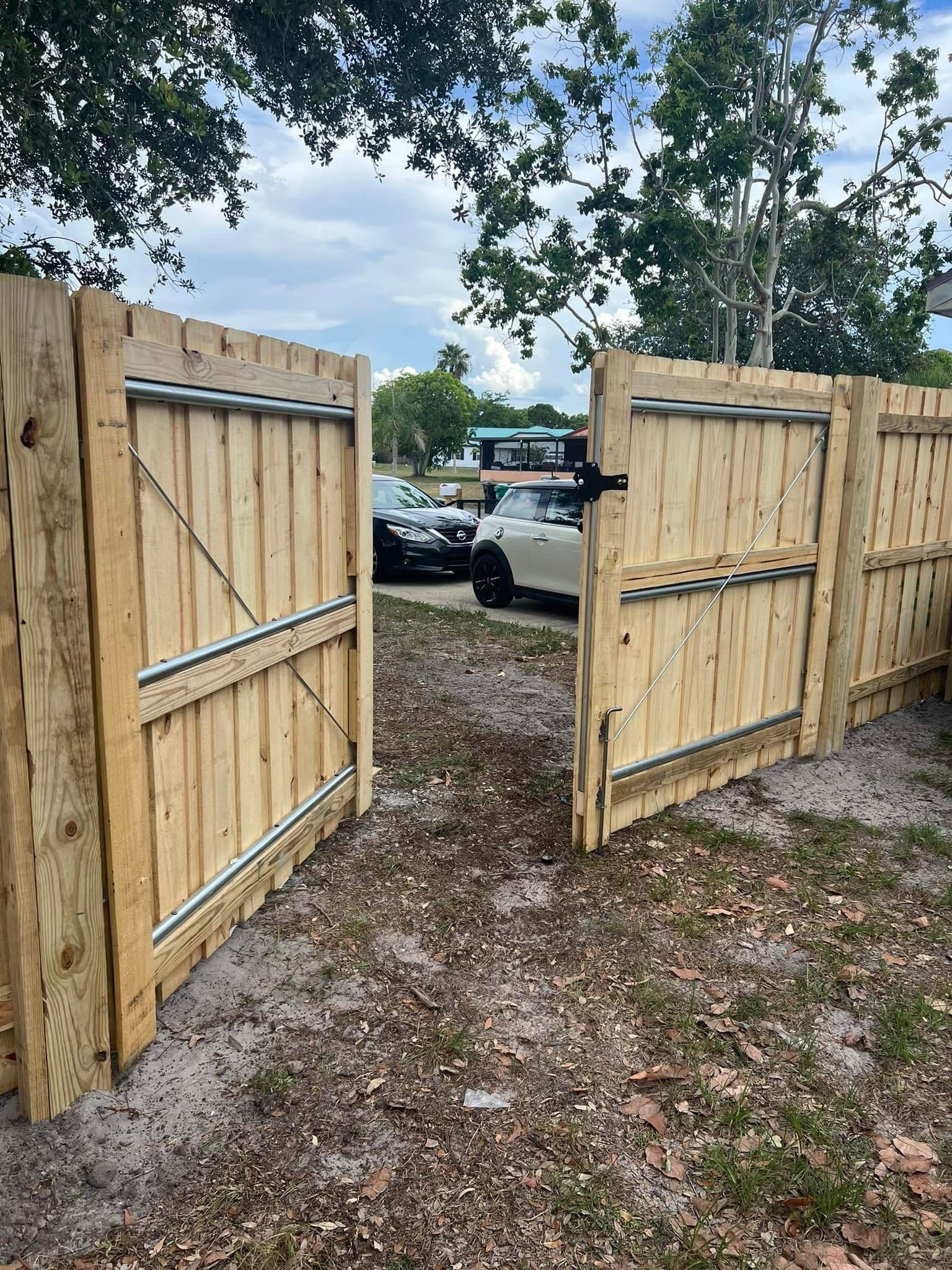 A wooden fence with a gate open and a car parked in the background.