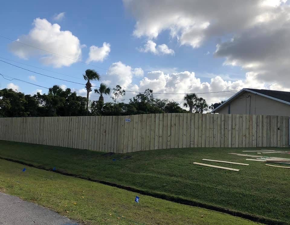 A wooden fence surrounds a lush green field in front of a house