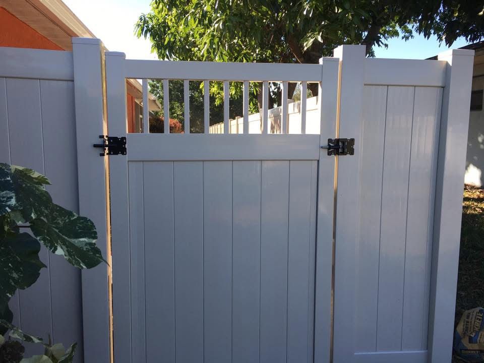 A white fence with a gate and a tree in the background.