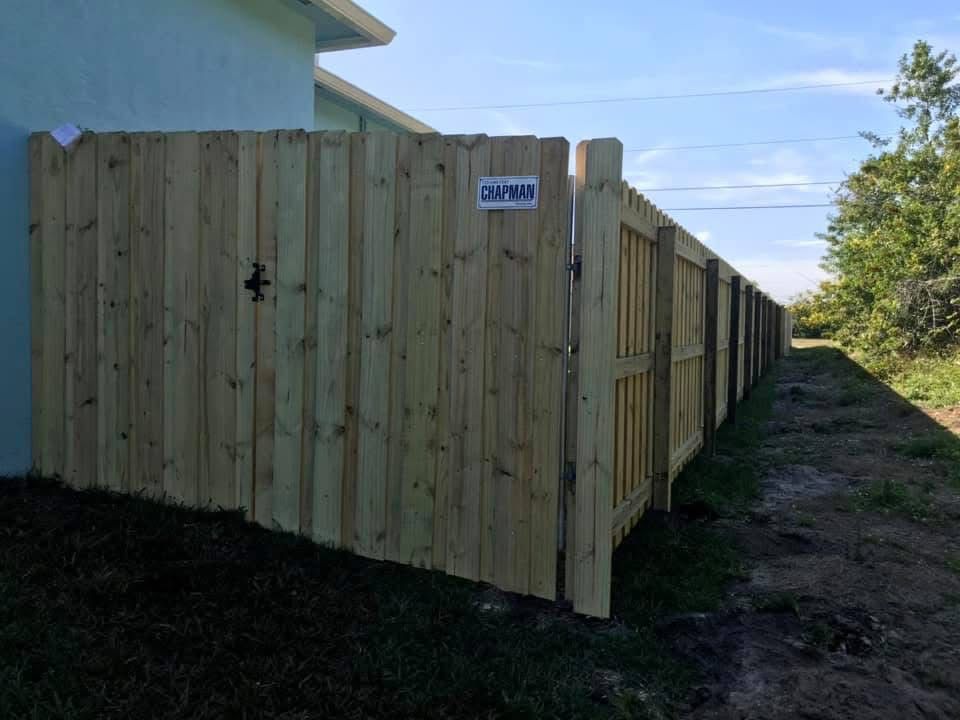 A wooden fence with a gate and a house in the background.
