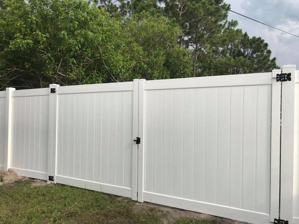 A white vinyl fence with a gate and trees in the background.