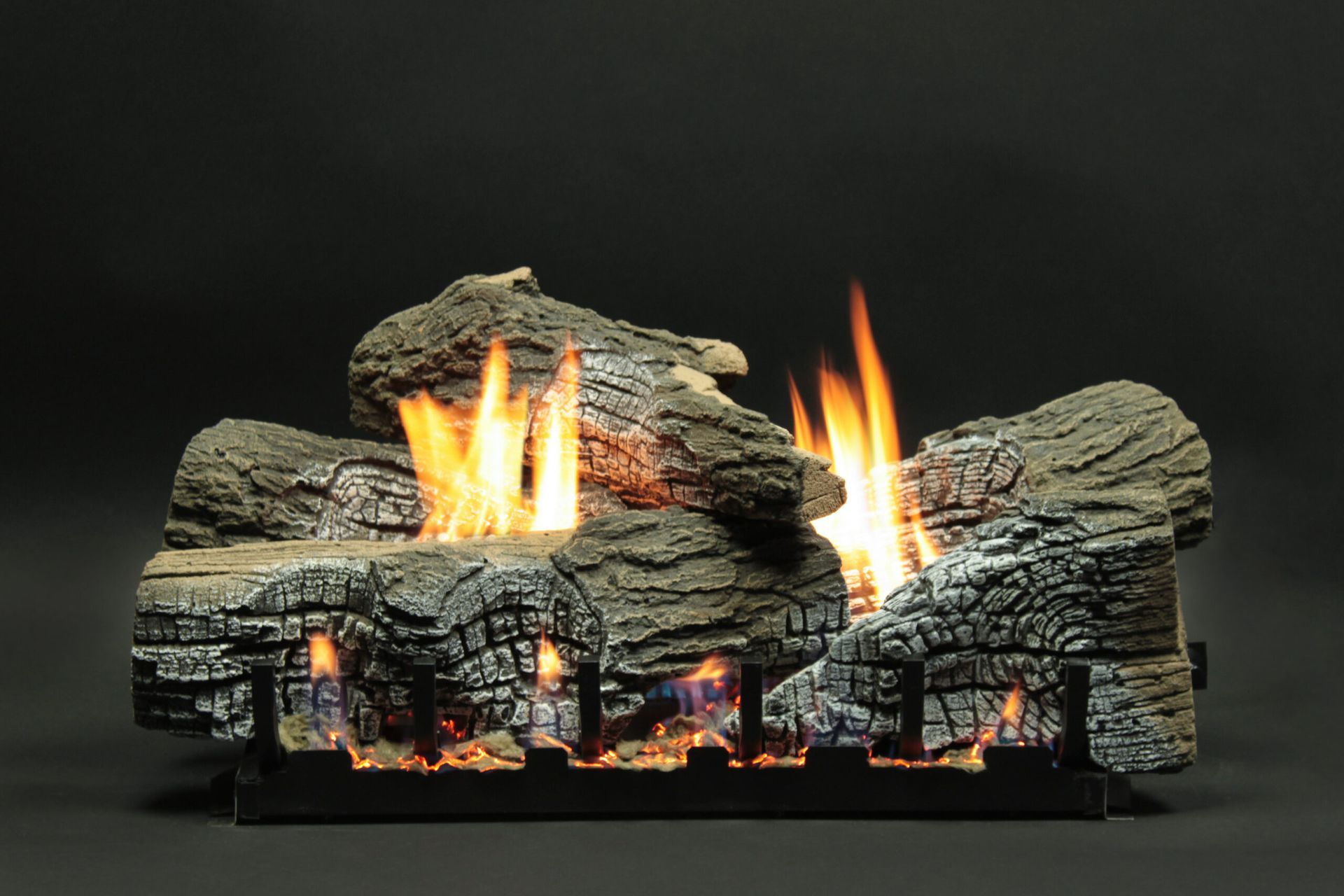 Gas fireplace logs with flames burning, on a black grate, set against a black backdrop.