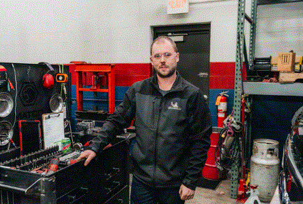 A man in a black jacket is standing in a garage.