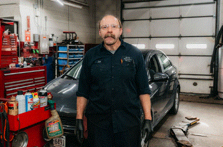 A man is standing in front of a car in a garage.