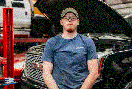 A man is standing in front of a truck with the hood up.