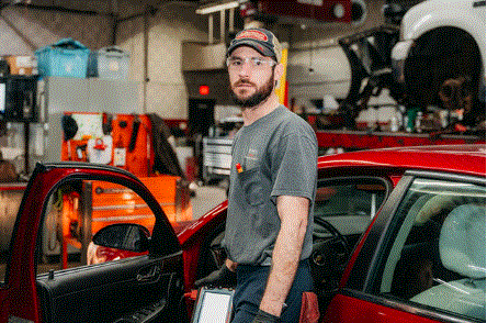 A man is standing next to a red car in a garage.