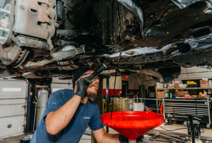 Mechanic draining oil from a car at an auto shop, using a wrench.