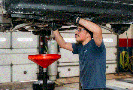 A mechanic working under a car, using a wrench. Oil drain pan below. Garage setting.