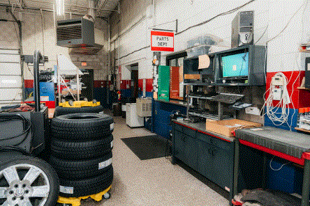 Man in a beanie and gloves uses a tablet near two computer monitors in an industrial setting.