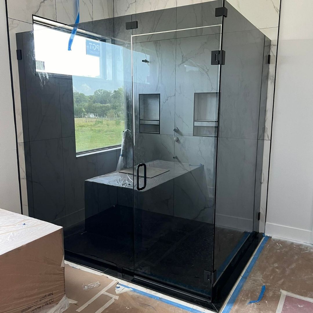 Modern glass shower enclosure with black hardware in a bathroom under construction