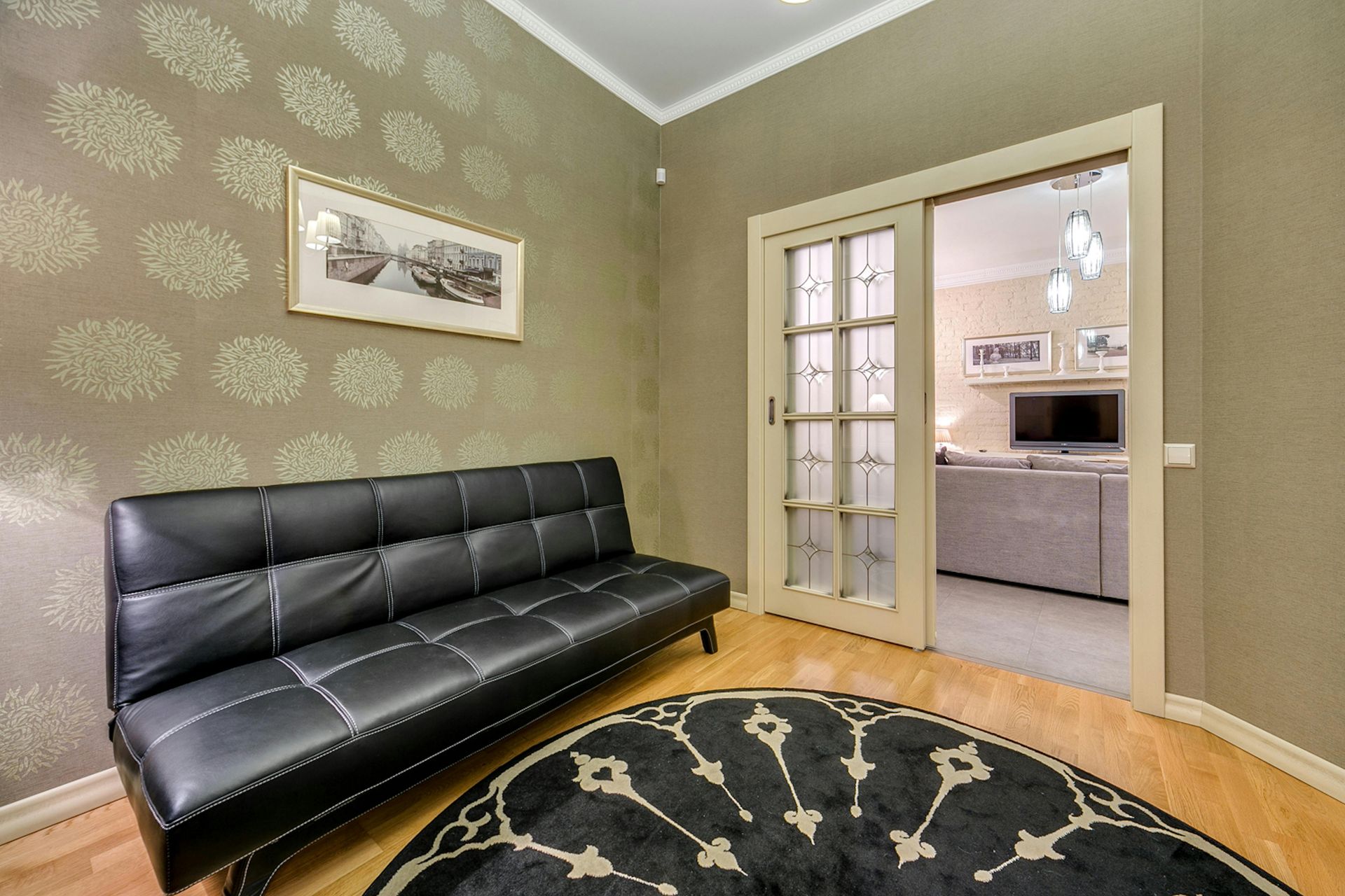A modern living space featuring a black leather sofa against patterned wallpaper, with a glass door leading to a room.