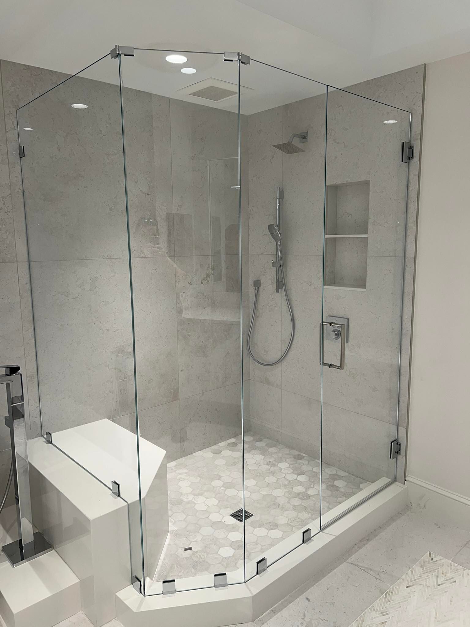 Glass-enclosed walk-in shower with marble tile, built-in bench, and handheld showerhead in a modern bathroom