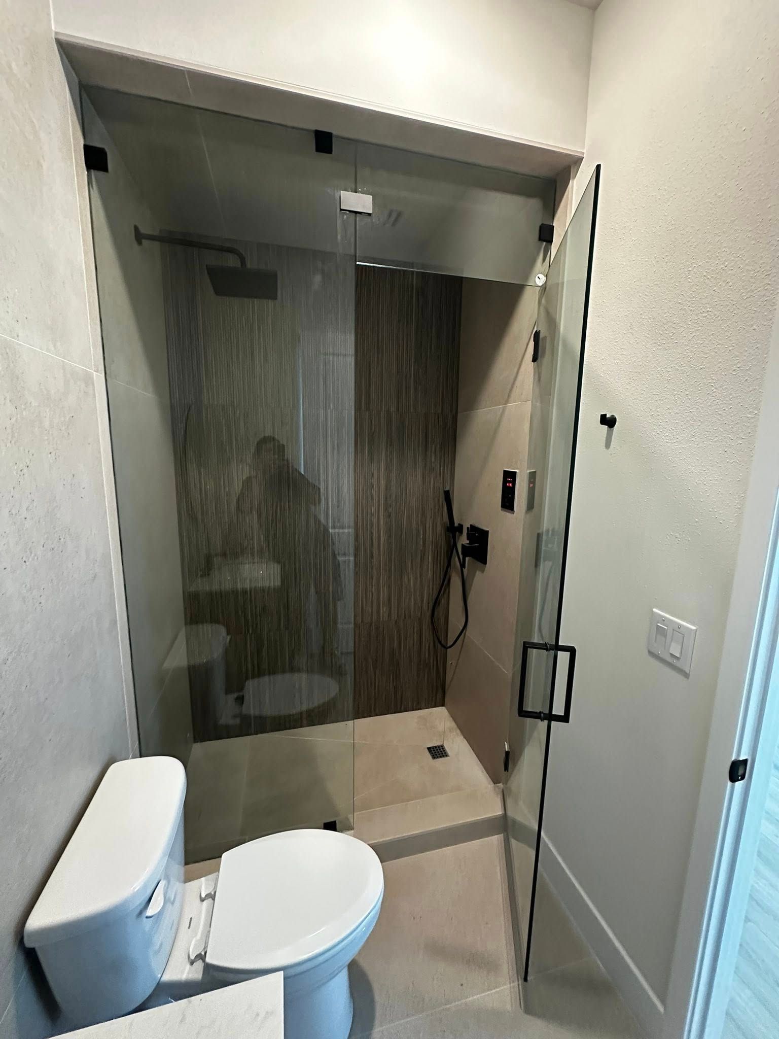 Small bathroom with toilet and glass-enclosed shower in a narrow alcove, viewed from the doorway.