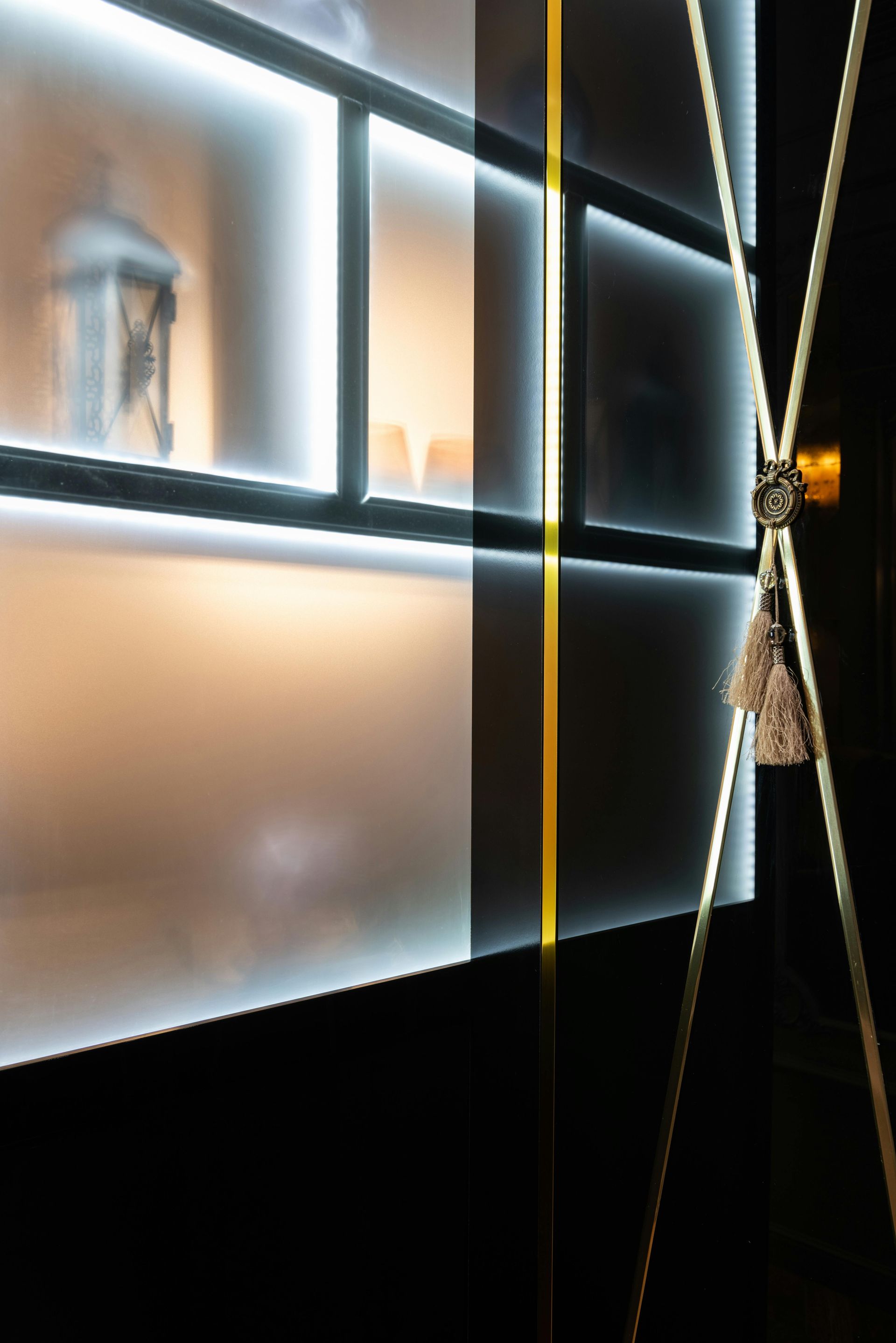 Illuminated shelves glow behind a frosted glass screen, beside a decorative gold cord with tassels.