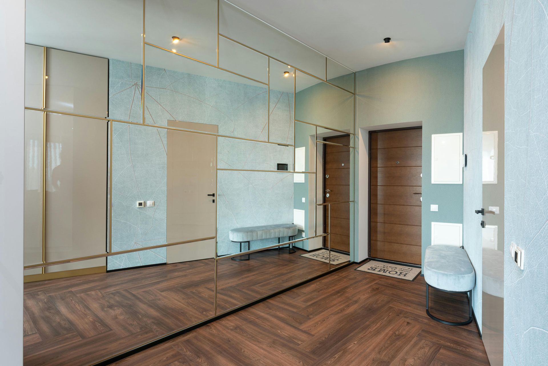A modern, light-filled entryway with wood-patterned flooring, blue-textured walls, and a large grid-patterned mirror.