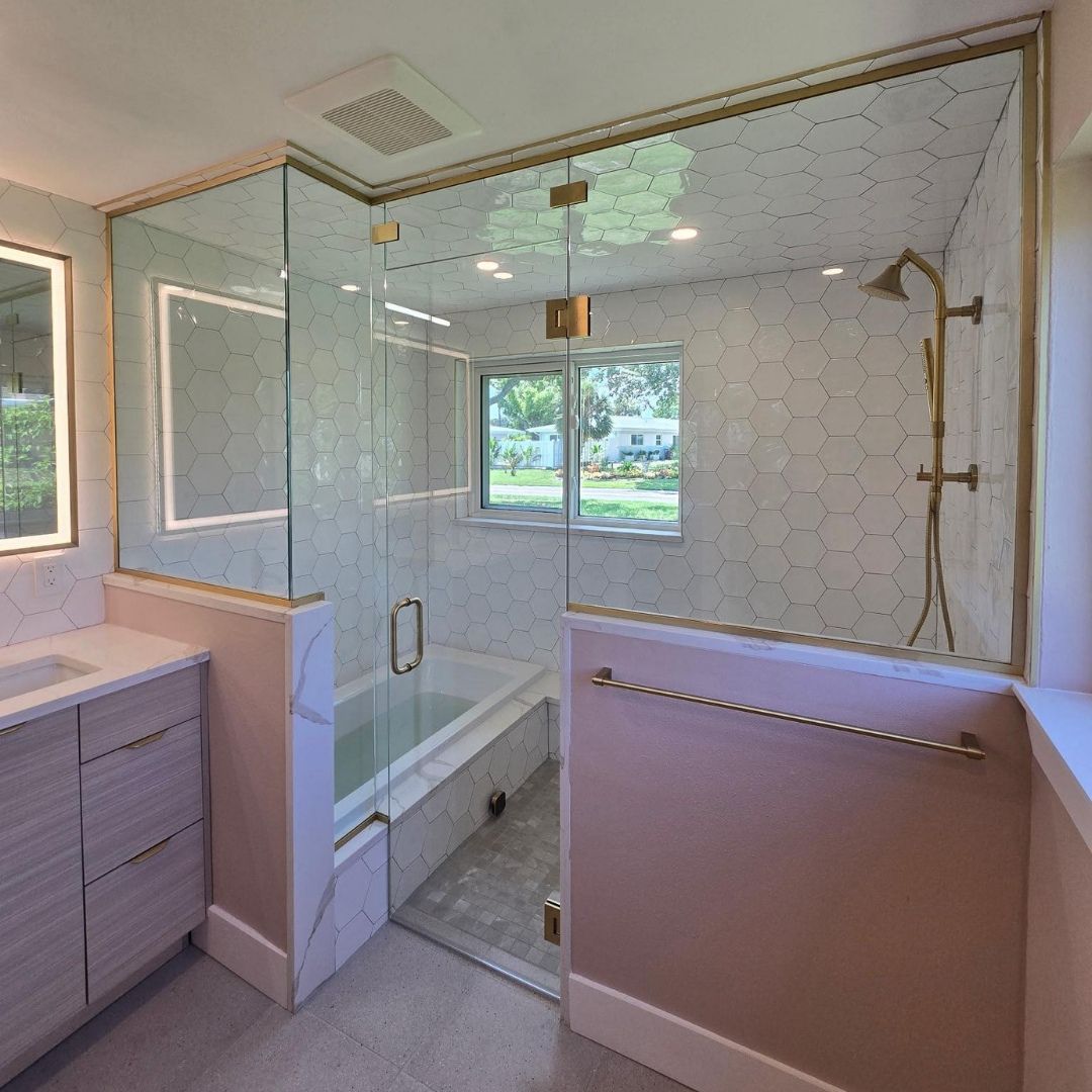 Bathroom with glass-enclosed shower, bathtub, and pink walls with gold trim