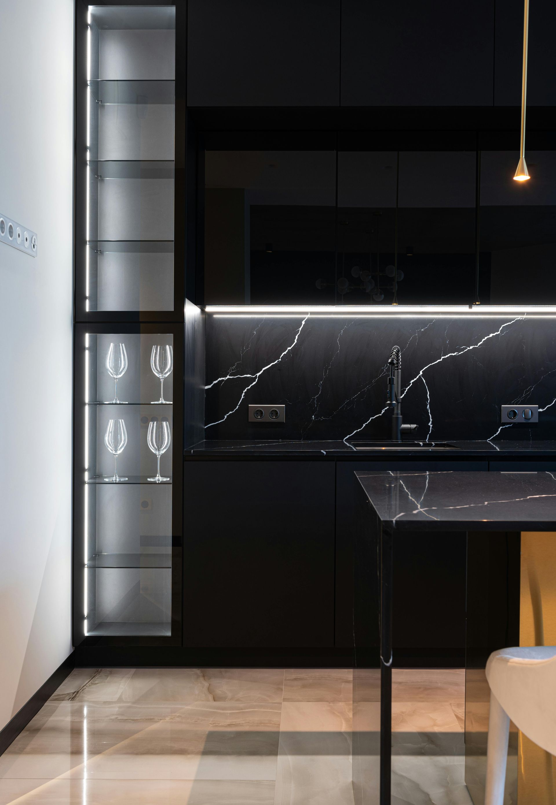 Modern dark kitchen with black marble backsplash, illuminated glass cabinetry, and a gold-accented island.
