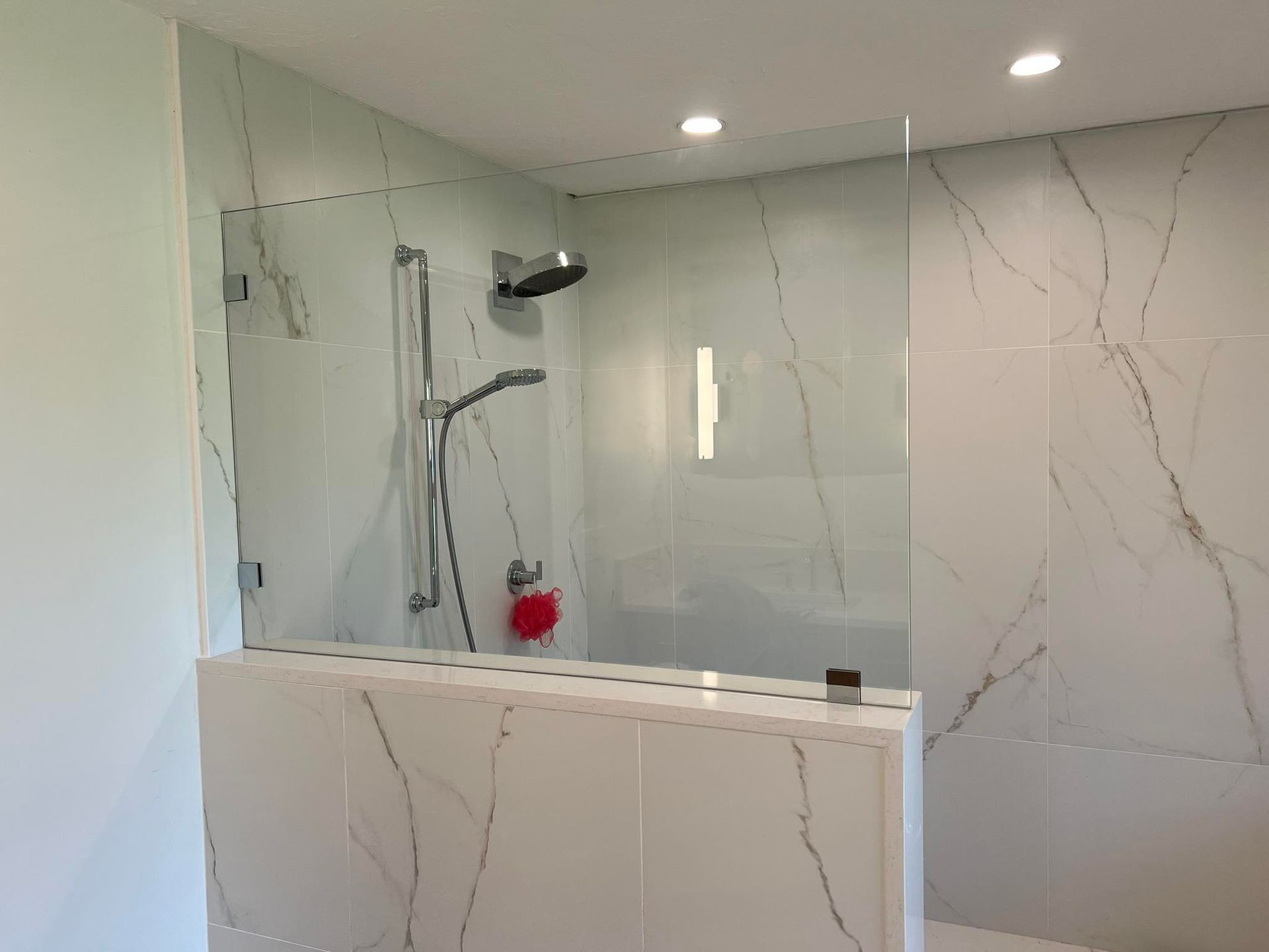 Modern bathroom shower with glass enclosure, marble-style walls, and a white vanity in the foreground
