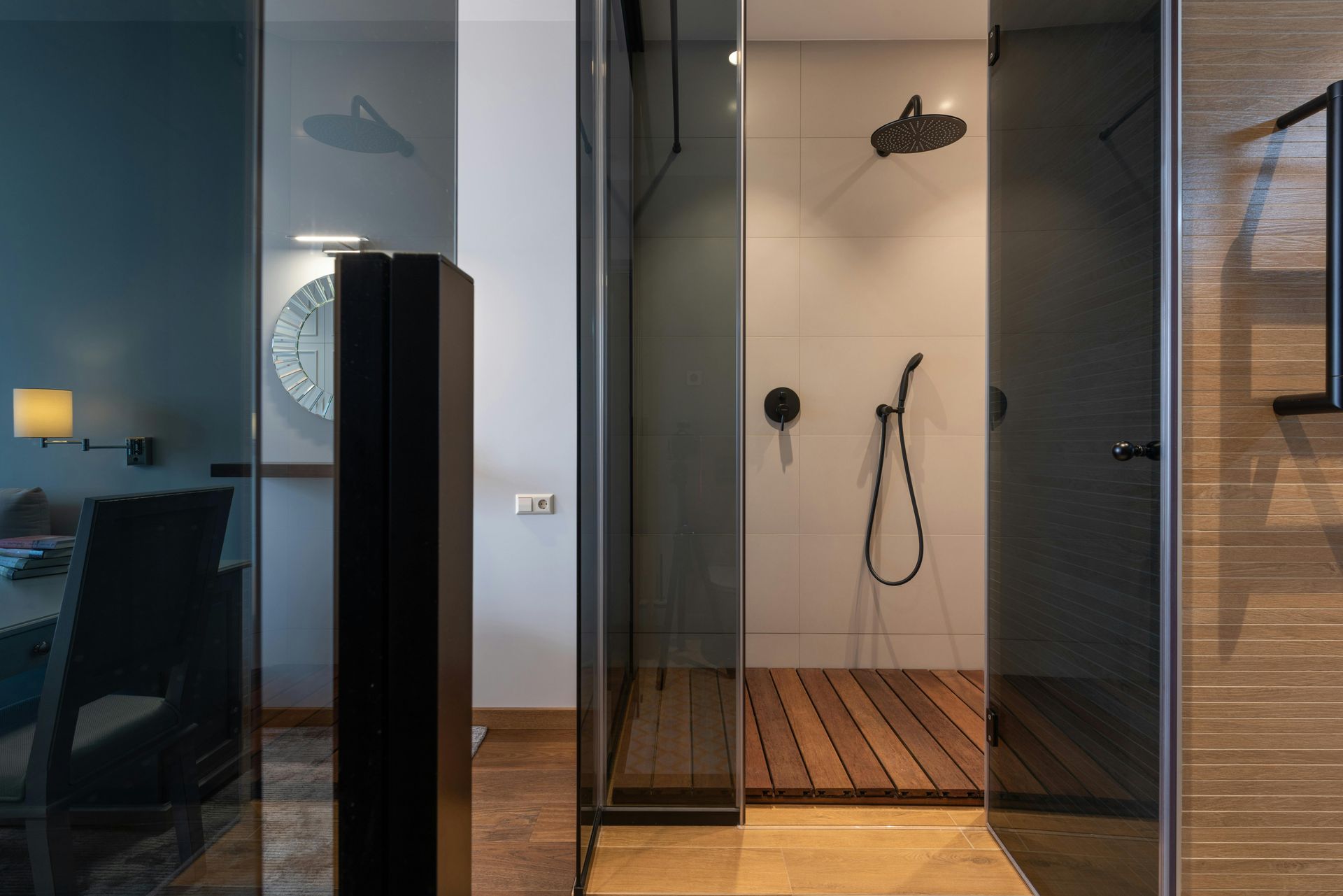 Modern bathroom interior with a glass-enclosed shower, wood slat floor, and dark fixtures against neutral tiled walls.