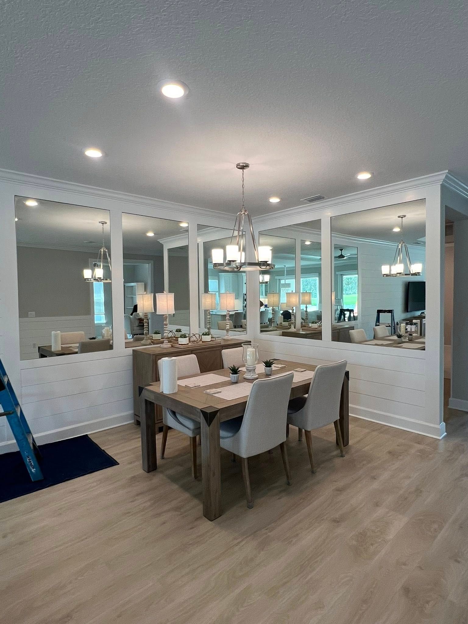 Bright dining room with white walls, wood table, chandelier, and mirrored wall panels