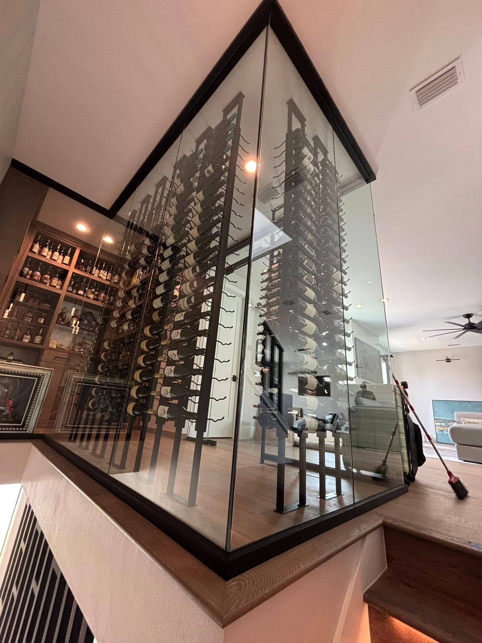 Modern staircase with glass railing, facing a wine display and bar seating in a contemporary interior