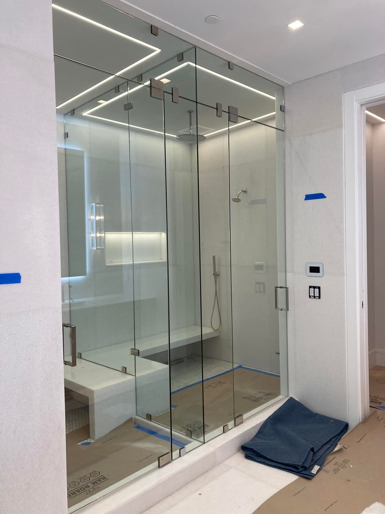 Glass-walled elevator lobby with modern white walls, mirrored panels, and a folded blue cloth on the floor.