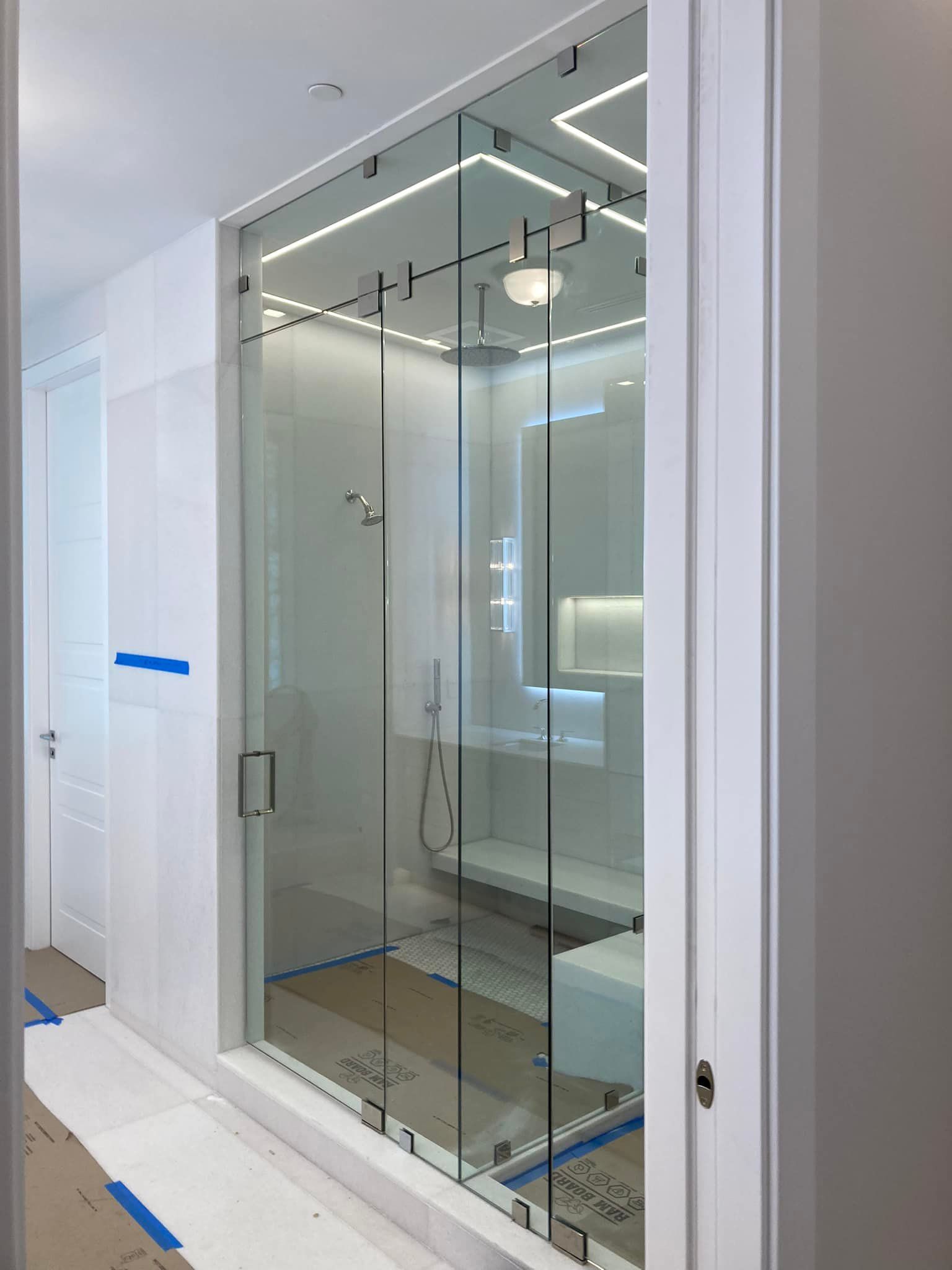 Glass shower enclosure in a bright, modern bathroom with white tile and chrome fixtures