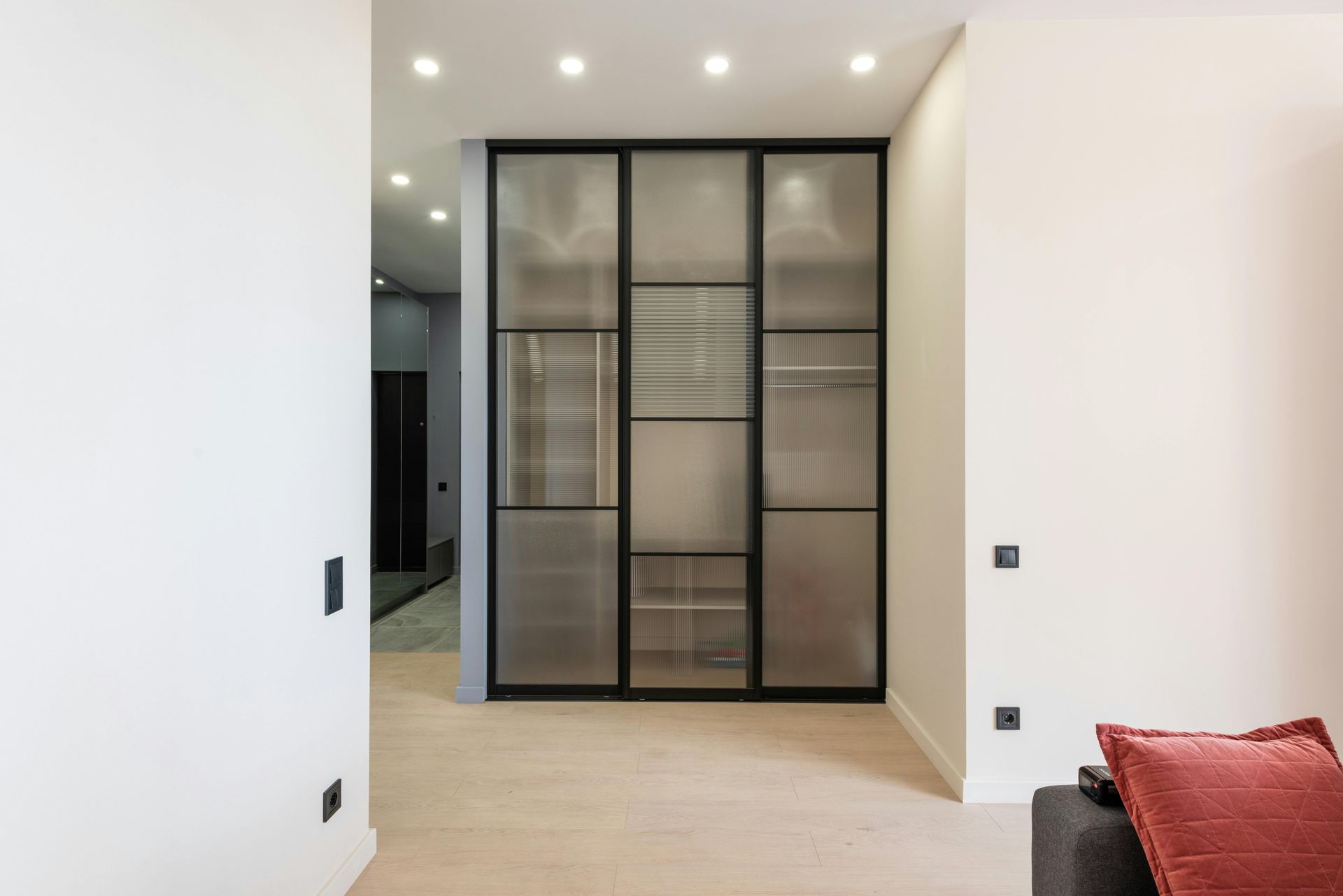 A modern walk-in closet with frosted glass doors, black metal frames, and built-in shelving, set in a minimalist room.