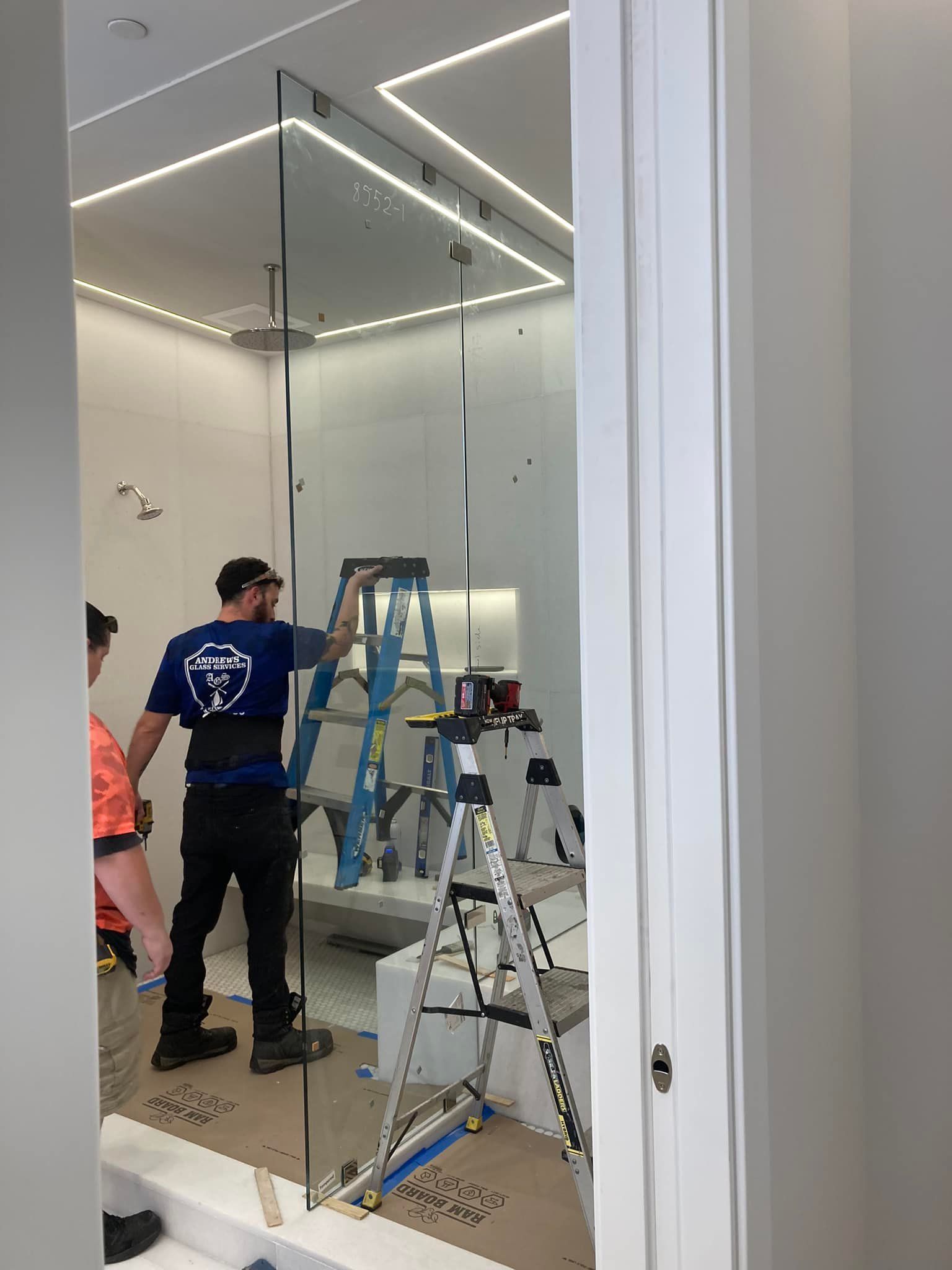 Workers installing a large glass mirror wall in a bright room with ladders and tools