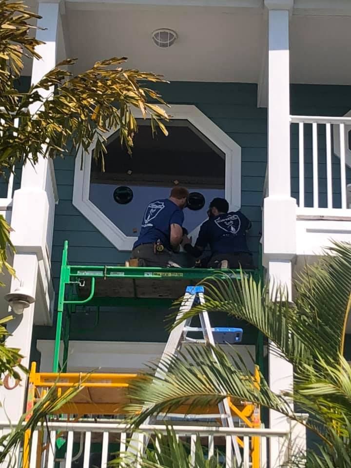 Two workers on a green scaffold repairing the front porch of a house with white columns and dark blue trim