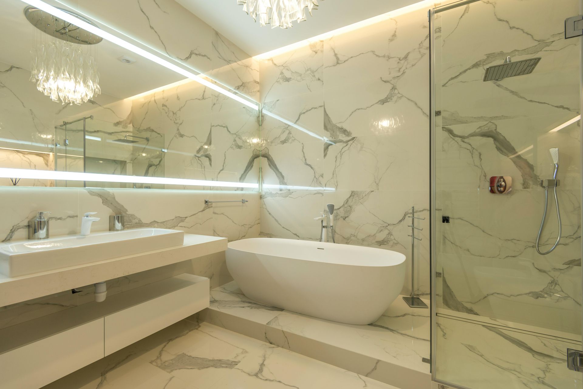A modern, luxury bathroom with white marble walls, a floating vanity, a freestanding oval tub, and a glass shower.
