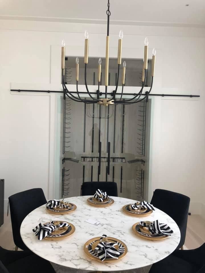 Modern dining room with round table set for six, black chairs, and a gold chandelier beneath a mirrored wall.