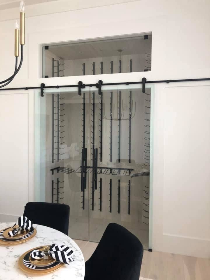 Modern dining room with a glass-front wine cellar behind a black sliding door and a set dining table in foreground