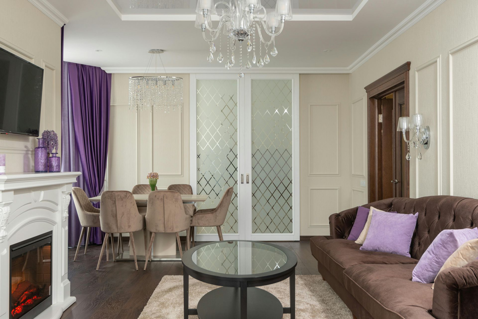 A living and dining room with a fireplace, brown sofa with purple pillows, dining table with chairs, and purple curtains.