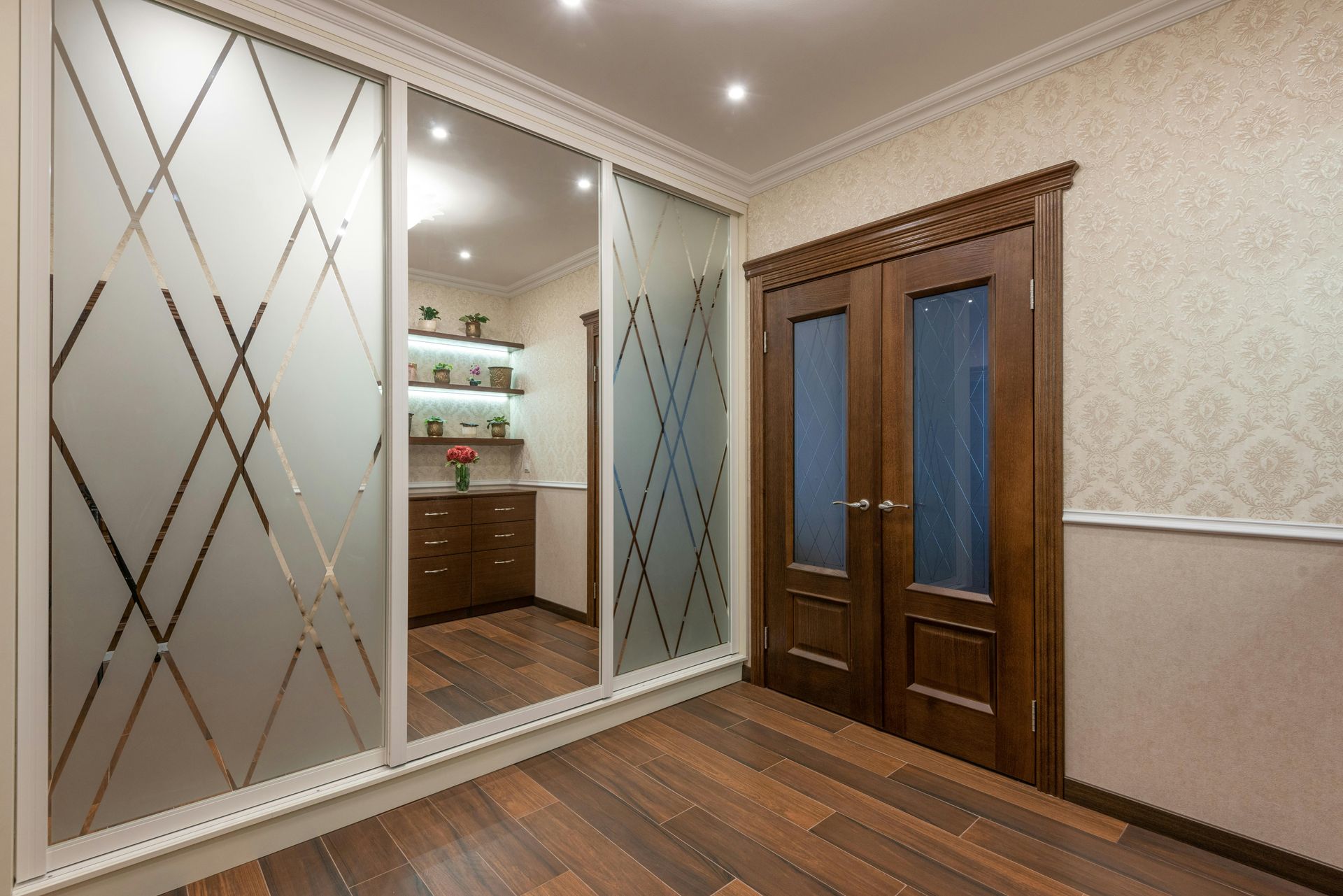 A hallway featuring a three-door sliding wardrobe with geometric mirrored patterns next to dark wood double doors.