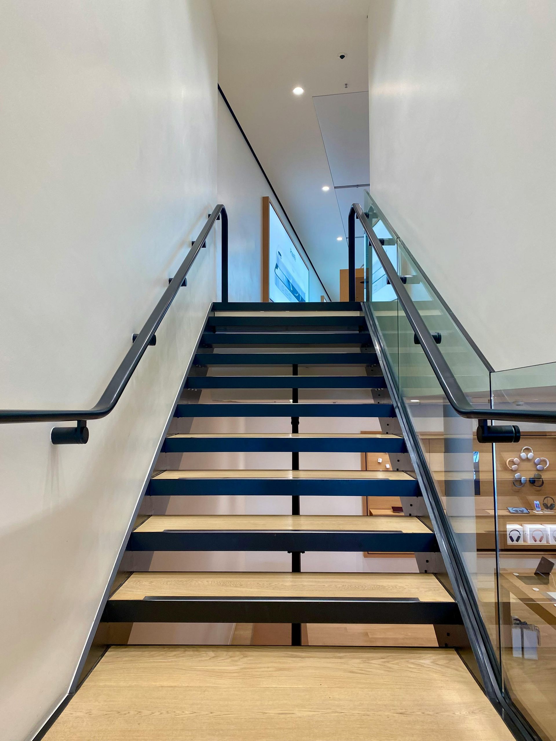 A straight staircase with light wood steps, black metal framing, and railings on both sides leads to an upper level.