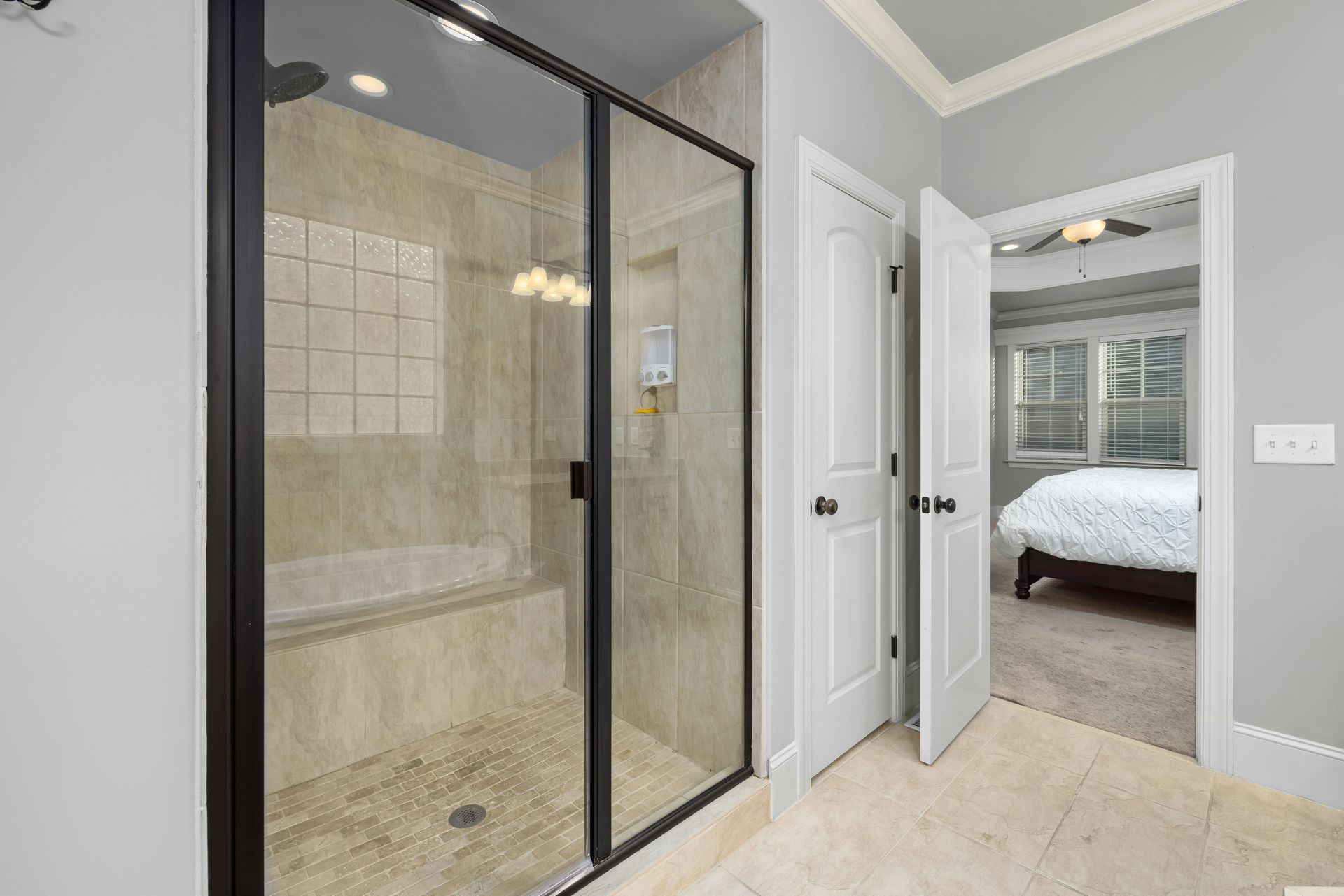A walk-in shower with black-framed glass doors next to an open doorway leading to a bedroom.