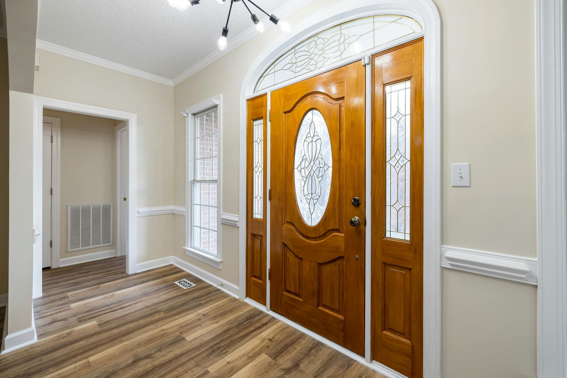 An entryway featuring a light-wood front door with an oval glass insert, side windows, and light hardwood-style floors.