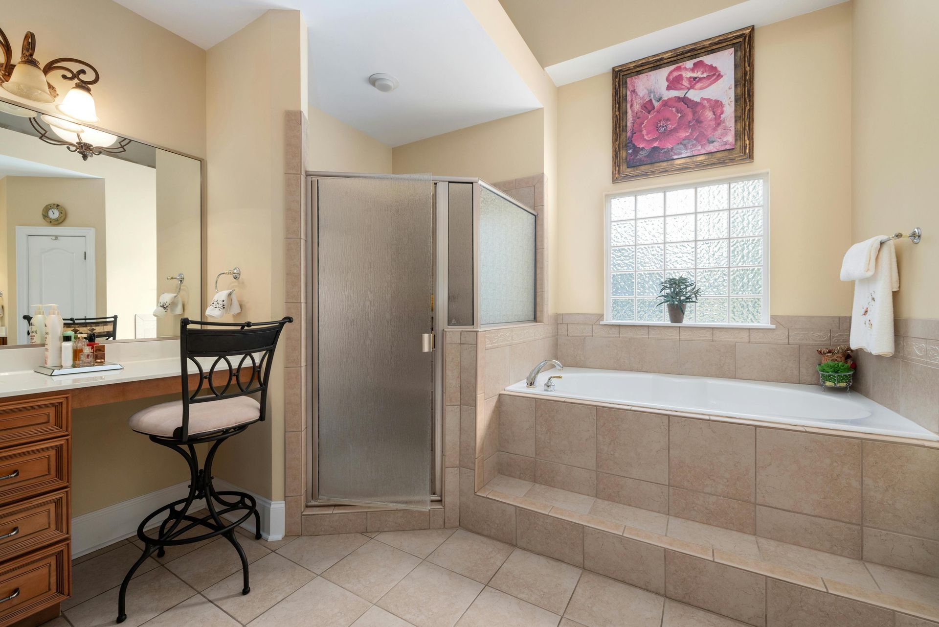 A bathroom with a vanity, tiled tub, glass-door shower, and a framed floral print on the wall.