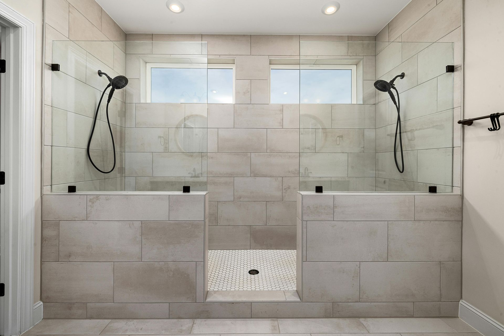 A modern walk-in shower with dual shower heads, neutral tiled walls, glass partitions, and a patterned tile floor.