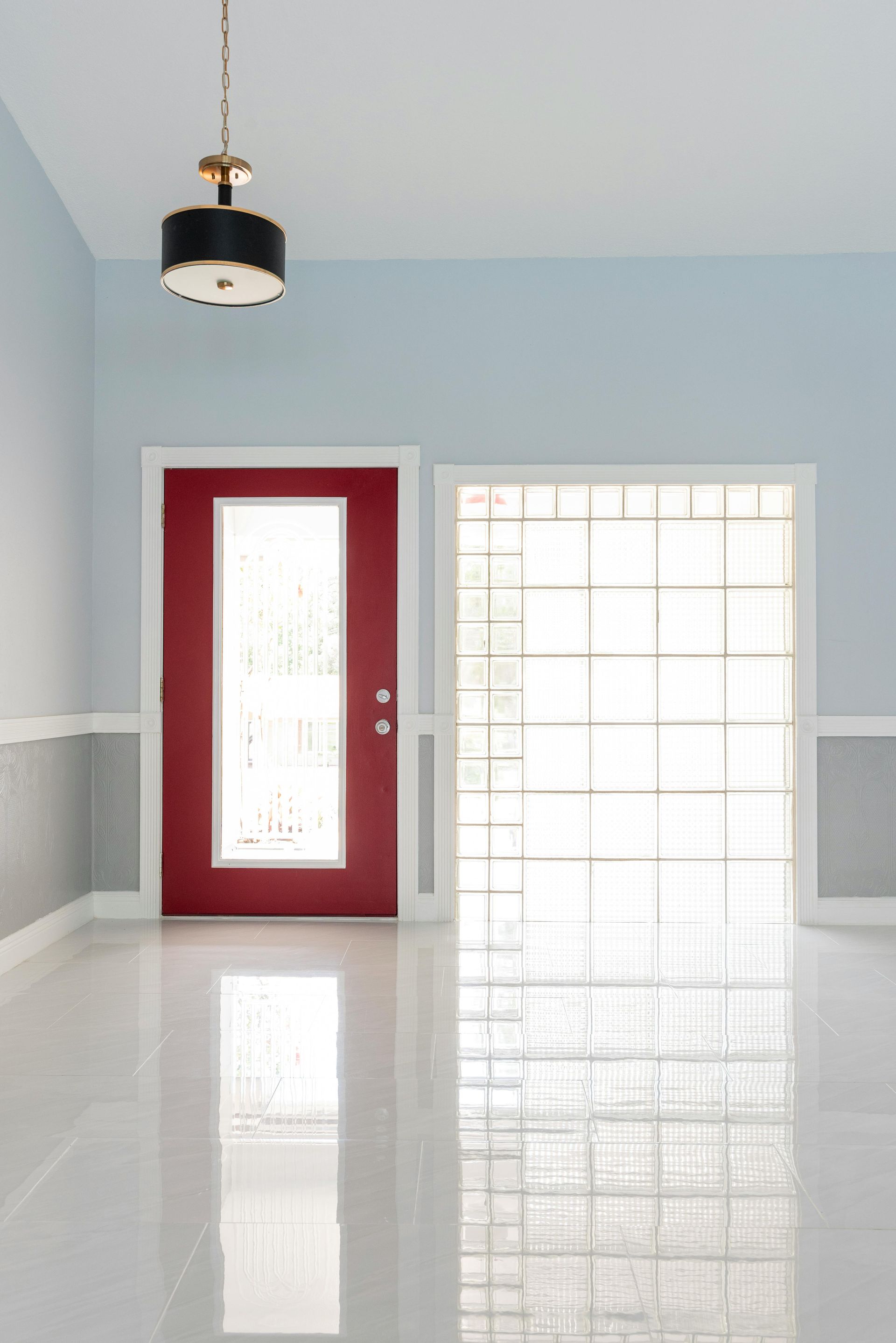 A red front door next to a glass block wall in an interior entryway with a pendant light and polished tile floor.