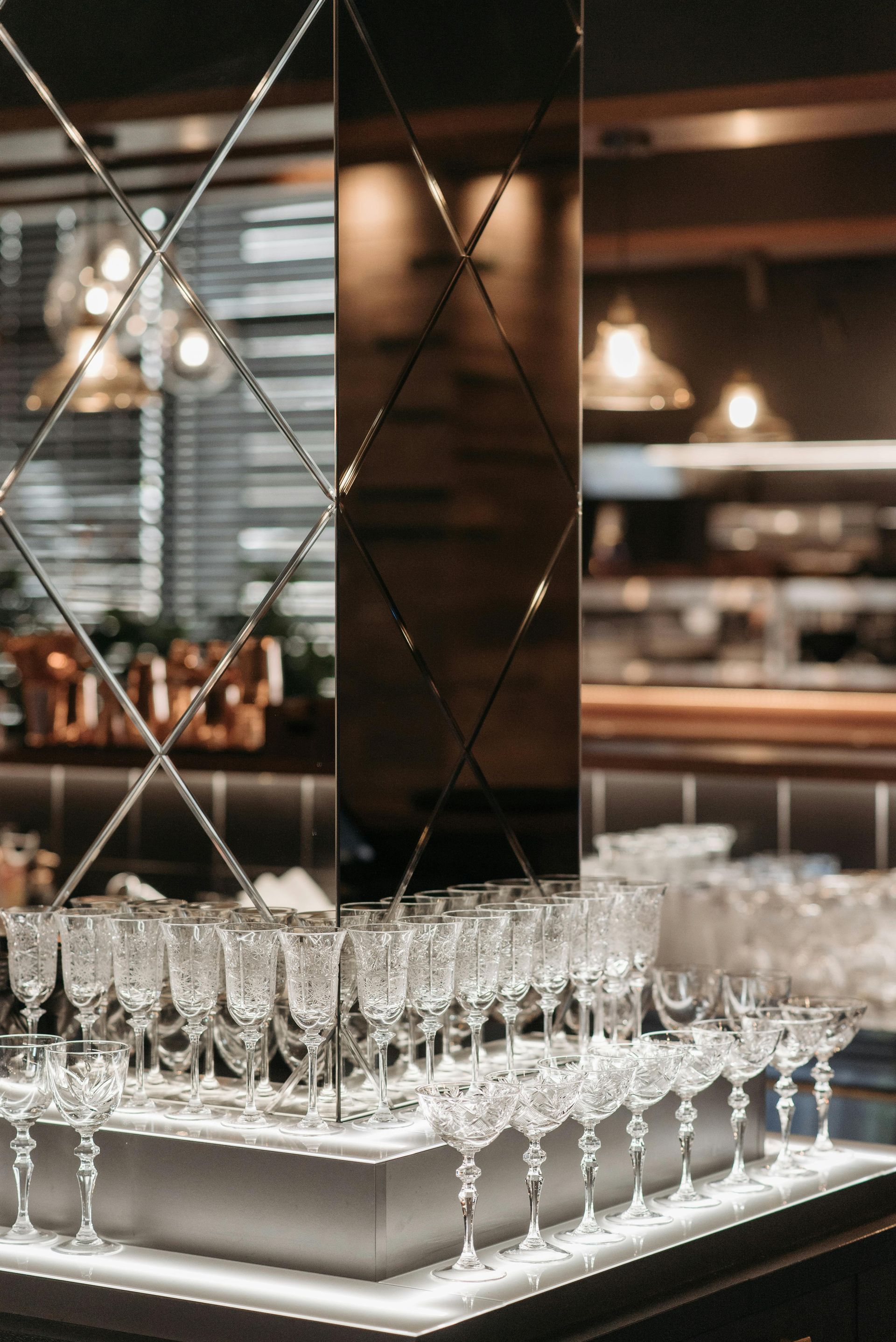 An array of crystal coupes and flutes arranged on a glowing display shelf in front of a diamond-patterned mirror.