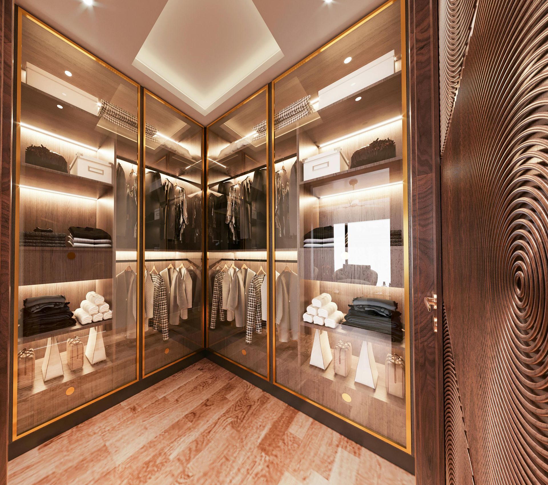 A modern, L-shaped walk-in closet with illuminated glass-front cabinets, wood flooring, and gold-trimmed shelving.