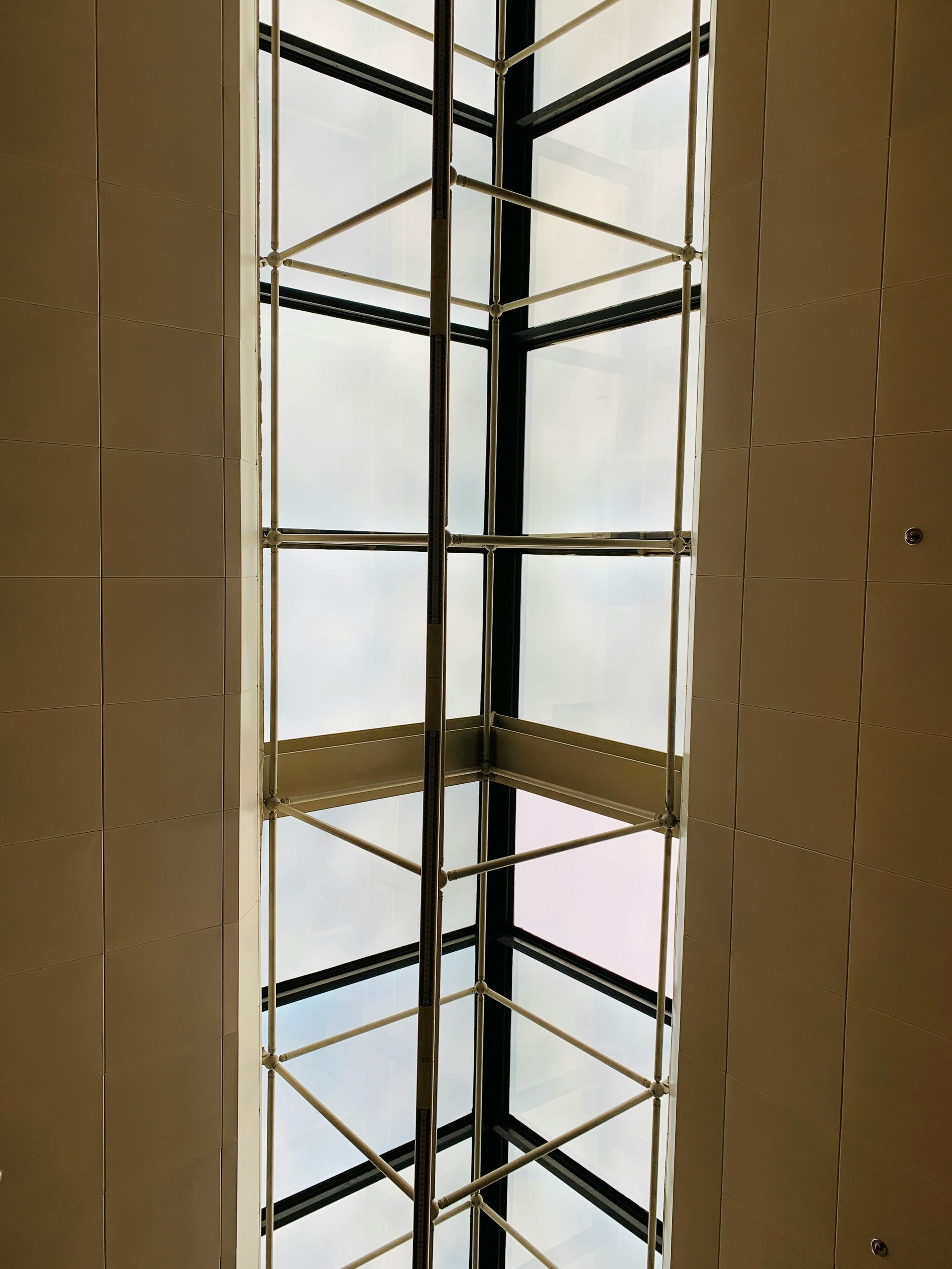 A low-angle view of a glass corner skylight framed by light-colored, paneled walls with a metal structural grid.