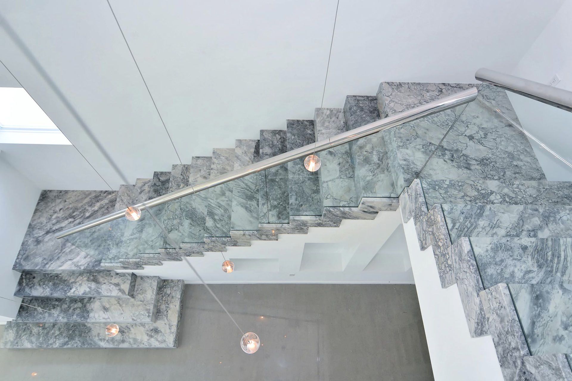Modern marble staircase with glass railing and pendant lights in a minimalist interior