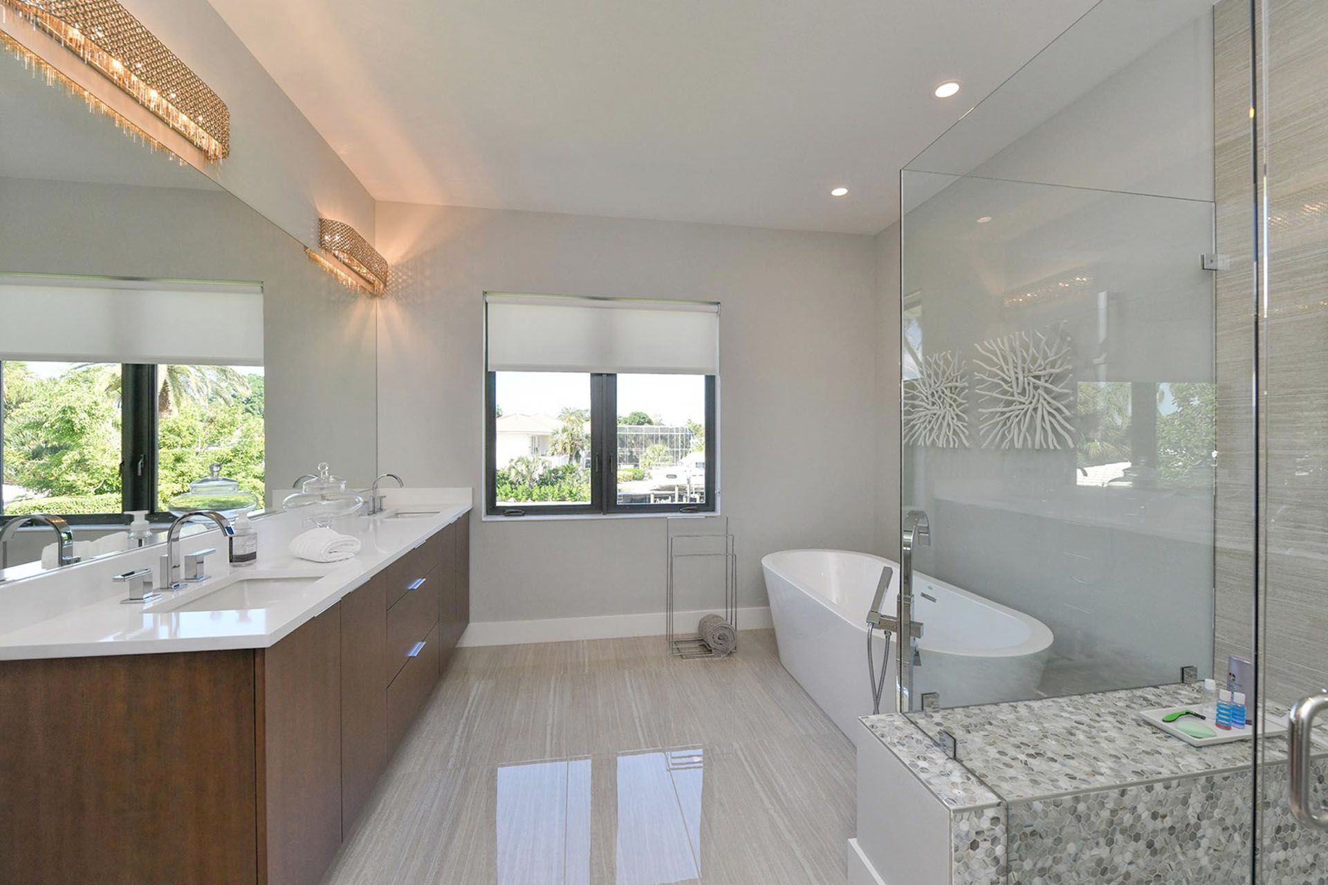 Bright modern bathroom with double vanity, large mirror, glass shower, and a freestanding tub by the window