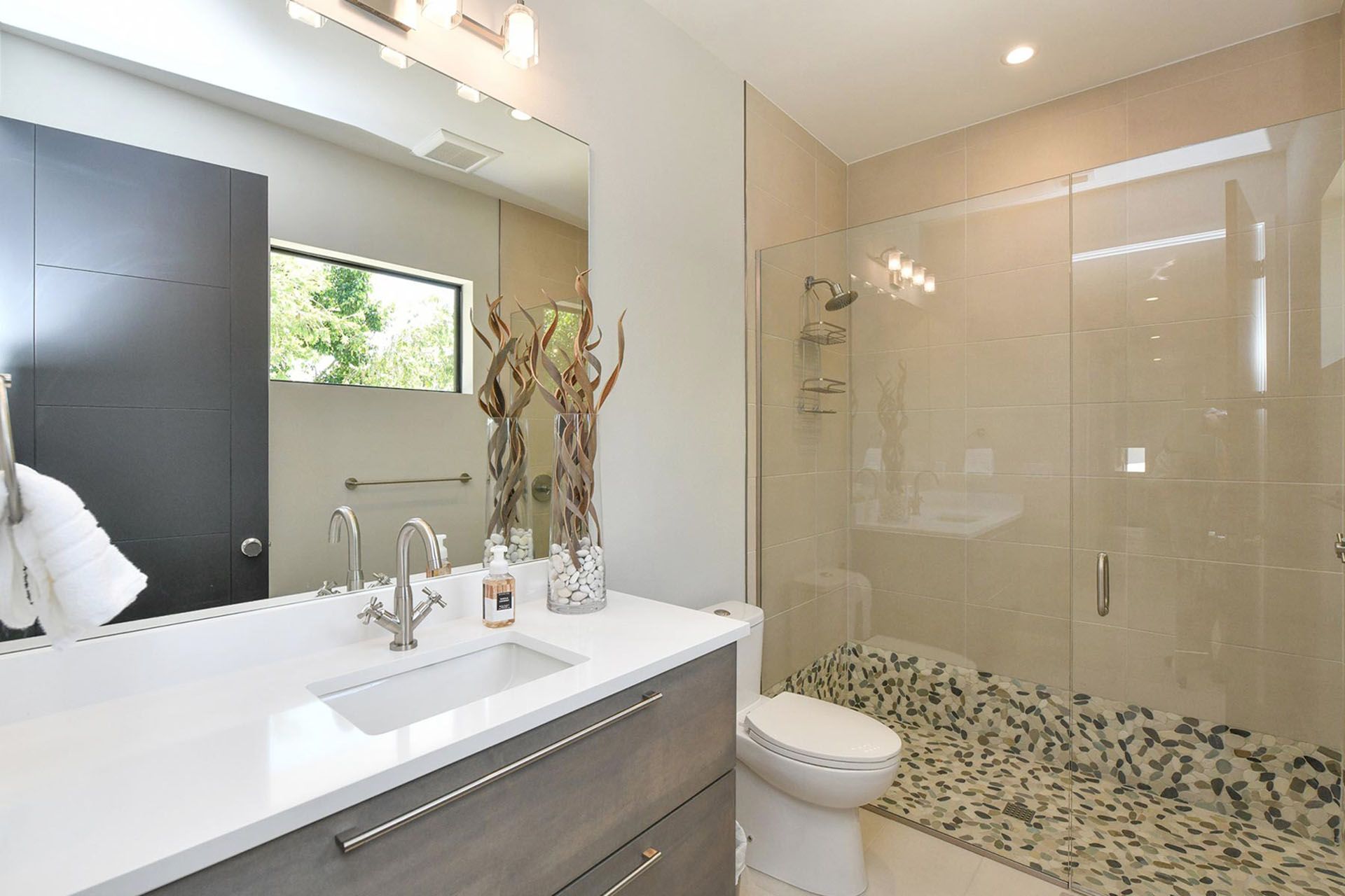 Modern bathroom with white vanity, large mirror, glass shower, and beige tile walls