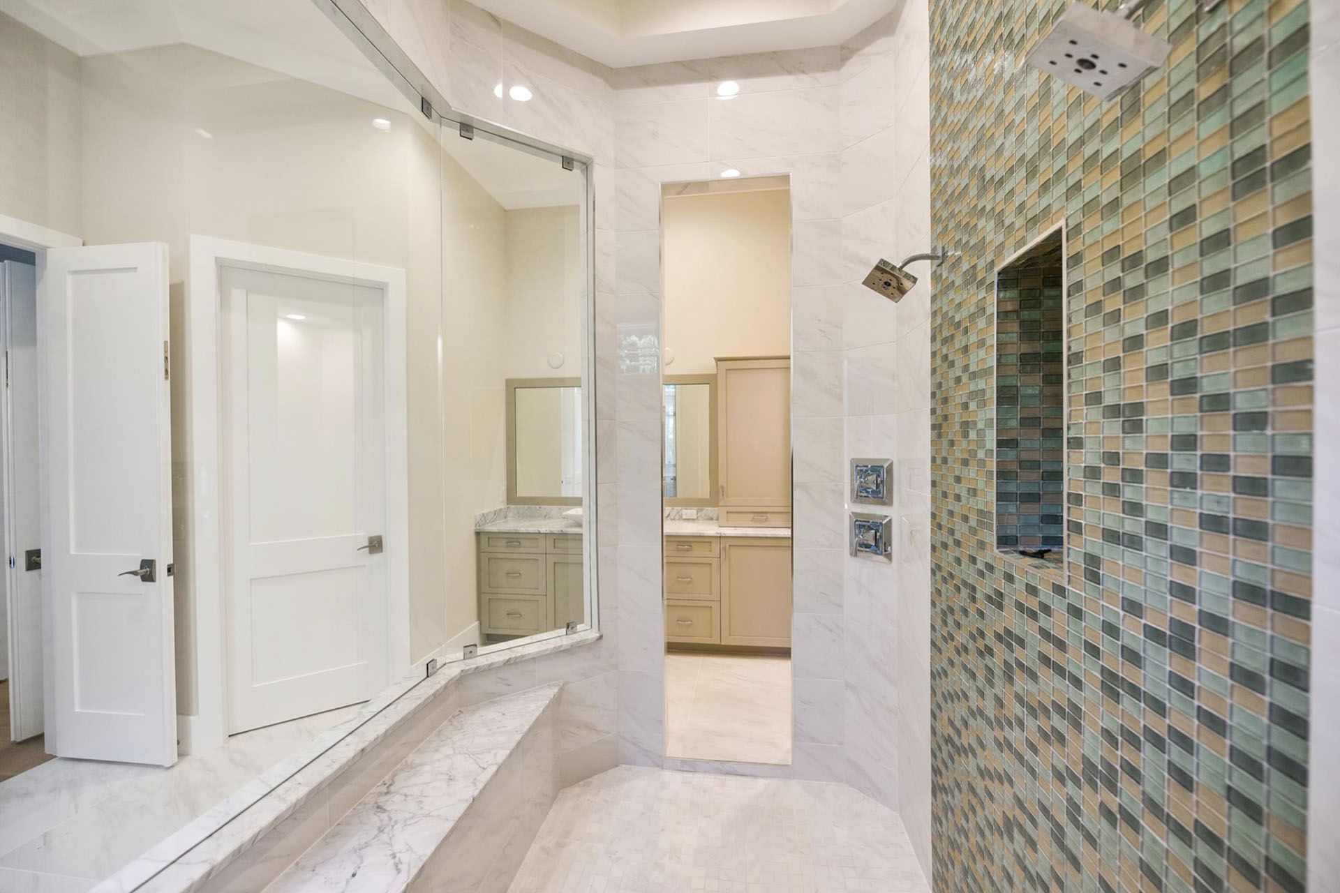 Modern bathroom with curved vanity, large mirror, white doors, and mosaic tile shower wall